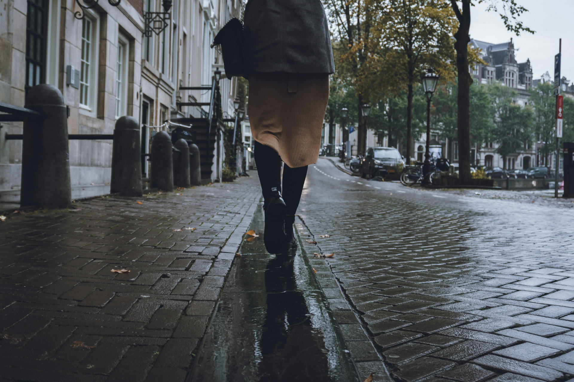 someone walking away down a wet cobbled street in a long coat on an overcast day